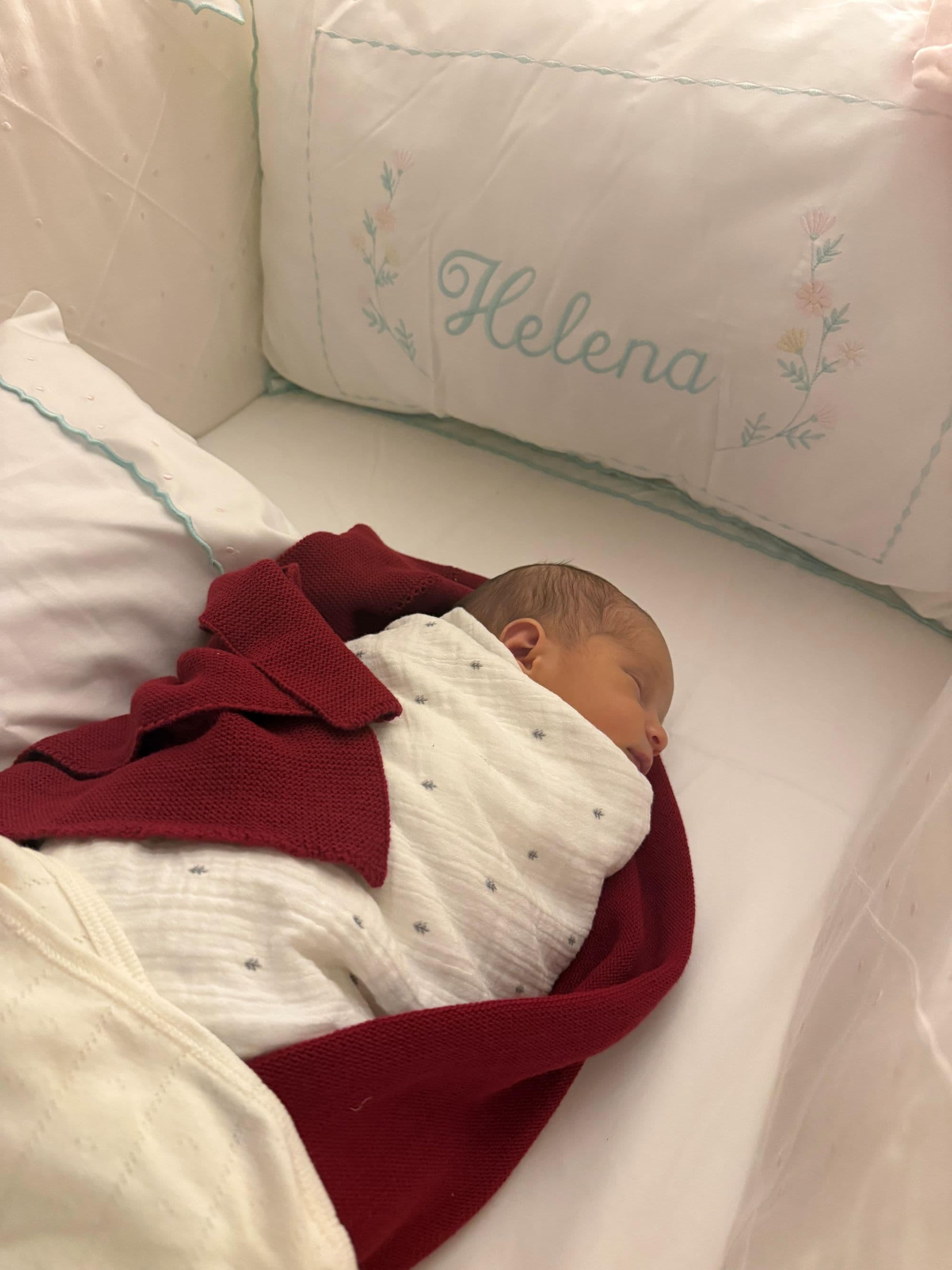 Baby Helena asleep in her crib, wrapped in a red knit blanket