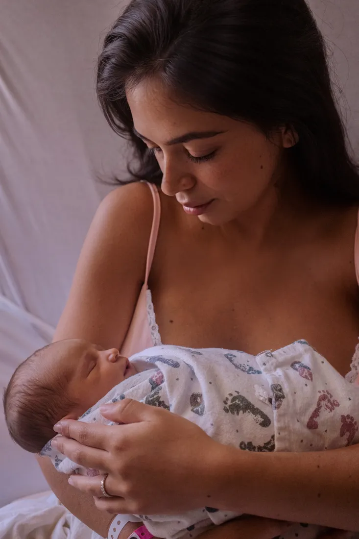 Nubia cradling newborn Helena in soft window light