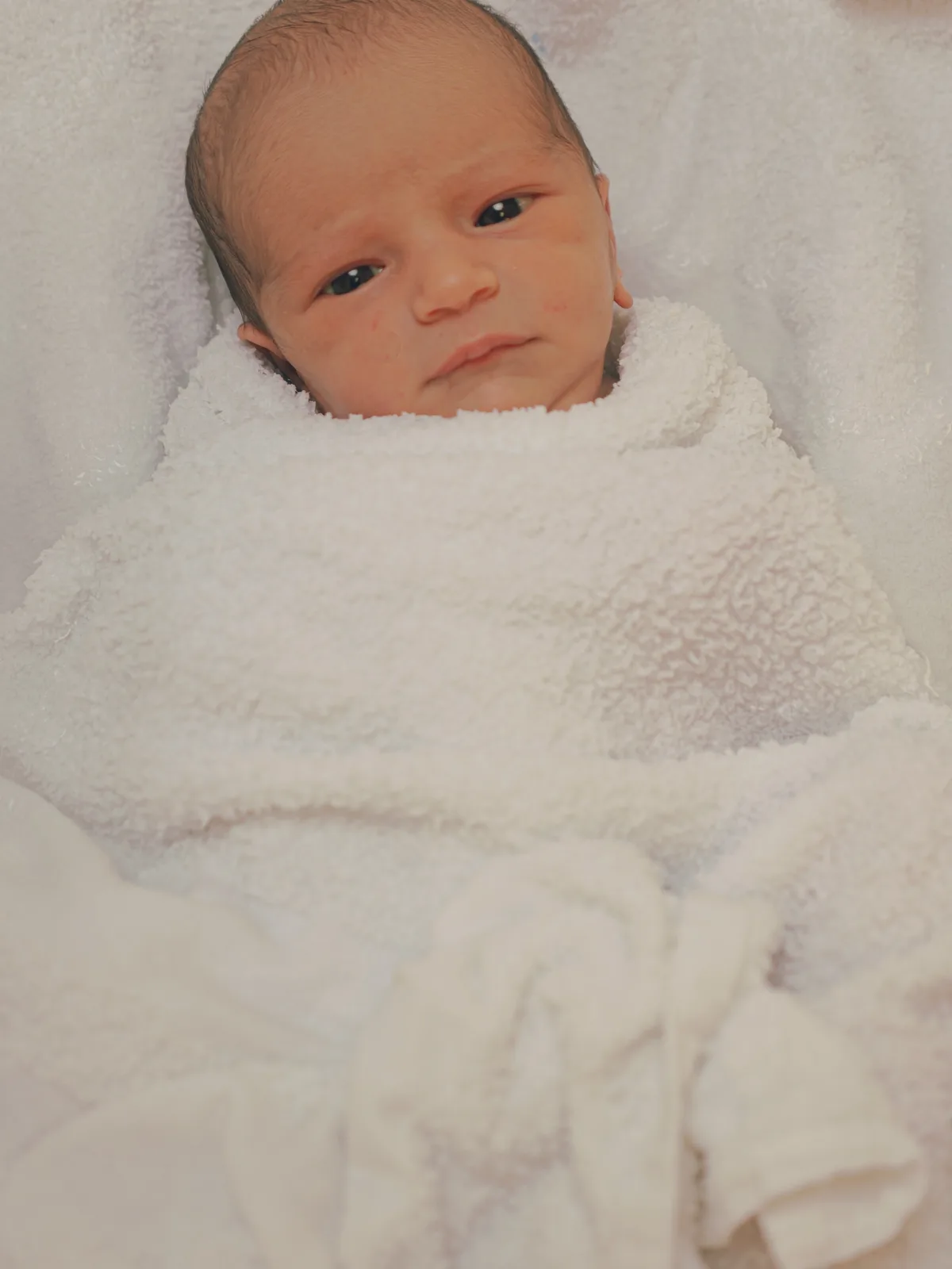 Baby Helena awake, wrapped in white, looking toward the camera